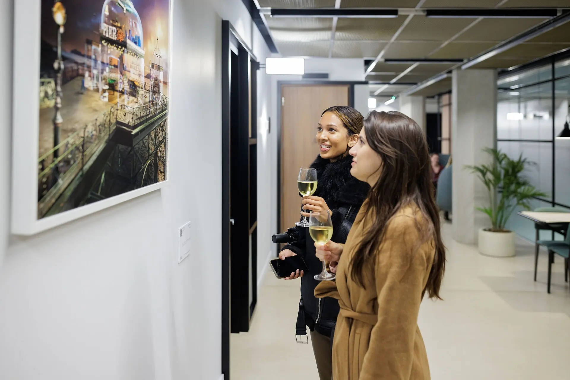 Two employees drink wine and discuss artwork.